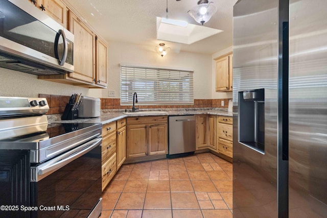 1019 Lee Ave NW, Palm Bay, FL 32907 - kitchen featuring light tile patterned floors, a sink, appliances with stainless steel finishes, light brown cabinetry, and a skylight