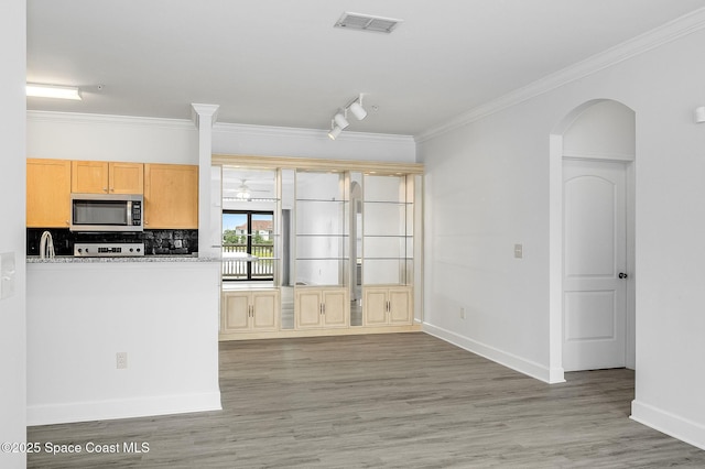 kitchen featuring stainless steel microwave, ornamental molding, light wood-style floors, visible vents, and arched walkways