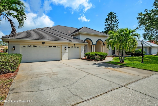 view of front of home with a garage, driveway, a front yard, stucco siding, and a tiled roof