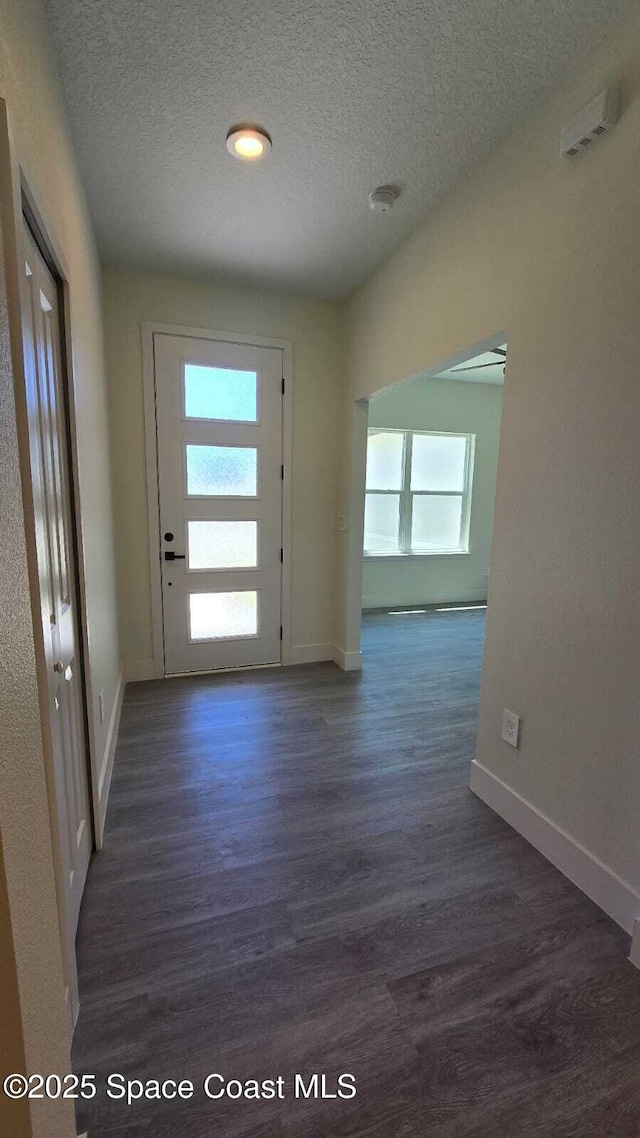 doorway with wood finished floors, a textured ceiling, and baseboards