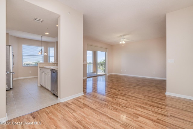 unfurnished living room with light wood-type flooring, a ceiling fan, visible vents, a sink, and baseboards