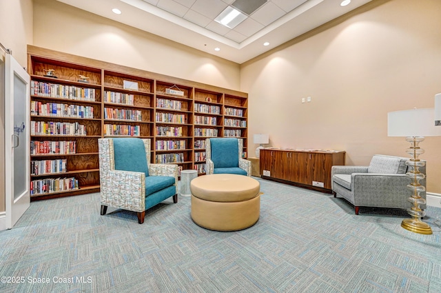 sitting room featuring carpet floors, recessed lighting, wall of books, and a towering ceiling