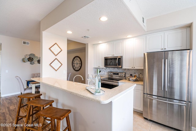 6838 Toland Dr Unit 307, Melbourne, FL 32940 - kitchen featuring stainless steel appliances, a breakfast bar area, white cabinets, a textured ceiling, and tasteful backsplash
