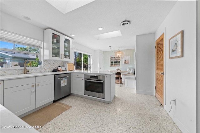 216 Cynthia Ln, Indian Harbour Beach, FL 32937 - kitchen with baseboards, light speckled floor, appliances with stainless steel finishes, a peninsula, and a skylight