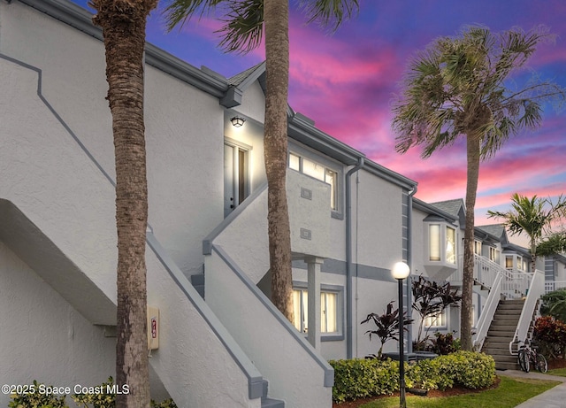 property exterior at dusk featuring stairway and stucco siding