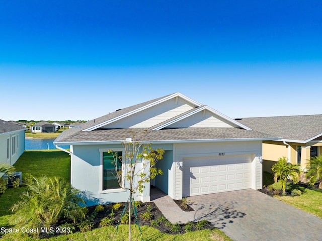 ranch-style home featuring an attached garage, decorative driveway, a shingled roof, and a front yard