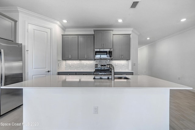 kitchen featuring a sink, stainless steel appliances, a center island with sink, light wood-style flooring, and visible vents