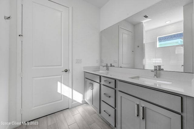 full bath with a tile shower, double vanity, visible vents, and a sink