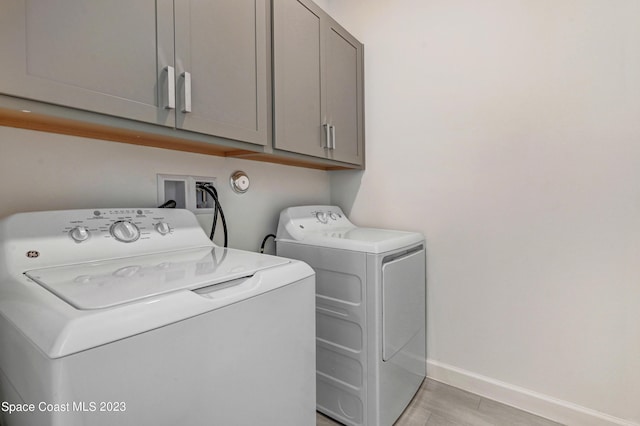 washroom featuring washing machine and dryer, baseboards, and cabinet space