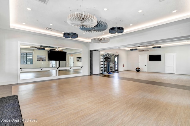 gym with a tray ceiling, visible vents, baseboards, recessed lighting, and wood finished floors
