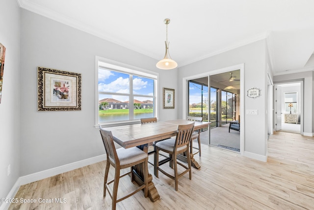dining room with baseboards, crown molding, light wood-style floors, and a water view