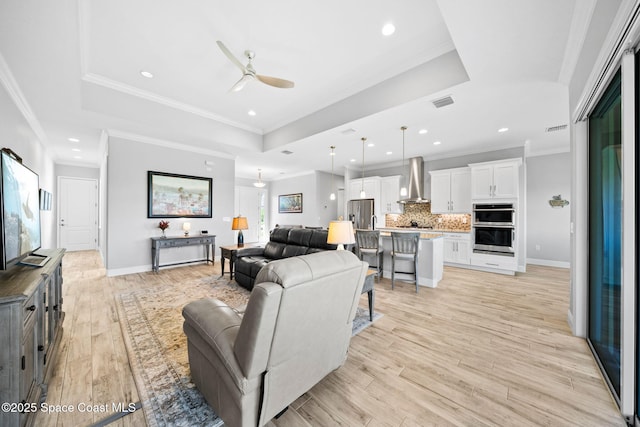 living area featuring a tray ceiling, light wood-type flooring, ornamental molding, and ceiling fan