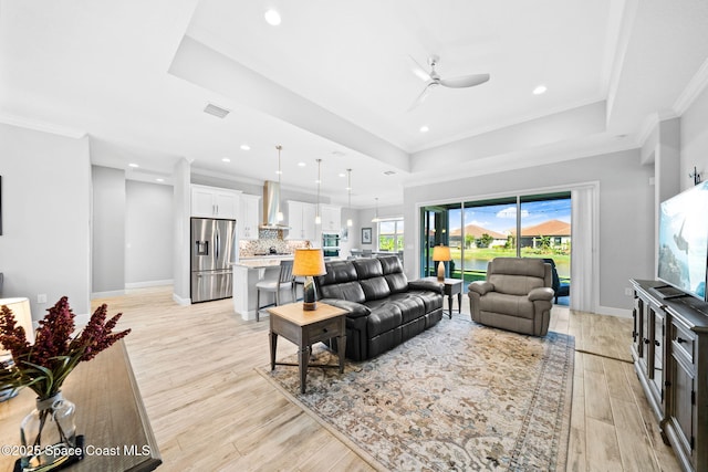 living room featuring light wood-style flooring, a tray ceiling, ceiling fan, and crown molding