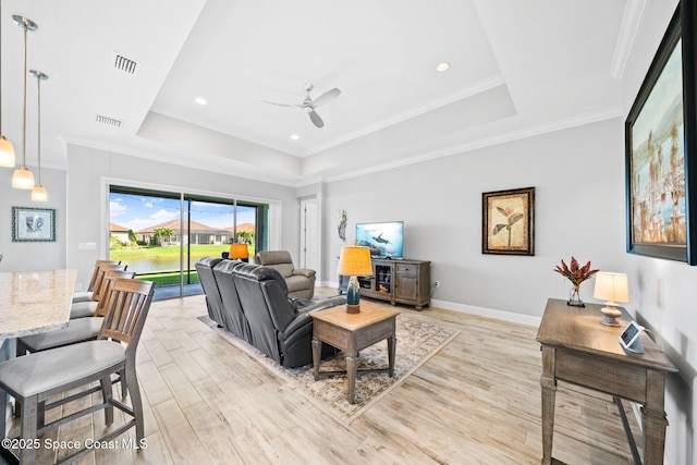 living room featuring a ceiling fan, a tray ceiling, light wood finished floors, baseboards, and visible vents