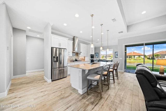 kitchen with wall chimney exhaust hood, a kitchen island with sink, a kitchen bar, stainless steel fridge with ice dispenser, and gas stovetop