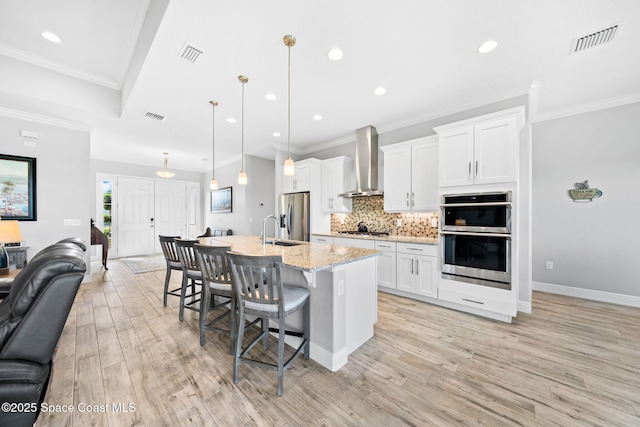 kitchen featuring wall chimney exhaust hood, open floor plan, stainless steel appliances, and visible vents
