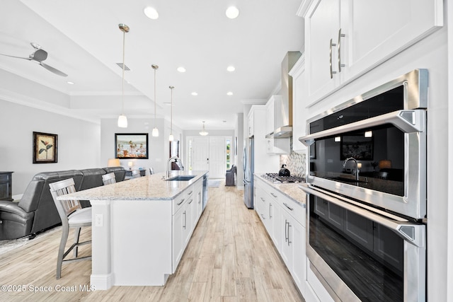 kitchen featuring stainless steel appliances, light wood-style flooring, open floor plan, white cabinetry, and crown molding