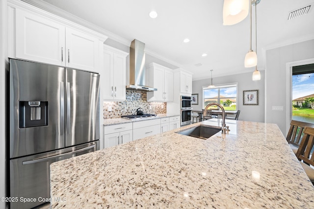 kitchen featuring wall chimney exhaust hood, a sink, visible vents, appliances with stainless steel finishes, and ornamental molding