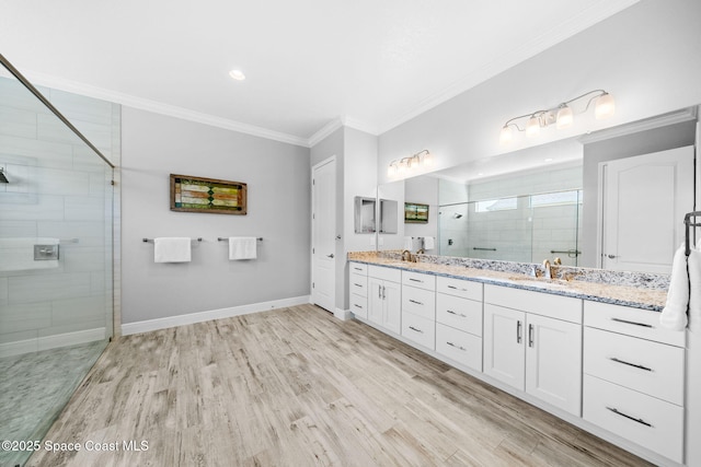 full bath with wood finished floors, a sink, a stall shower, double vanity, and ornamental molding