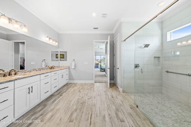 bathroom featuring double vanity, wood finished floors, ornamental molding, a sink, and a stall shower