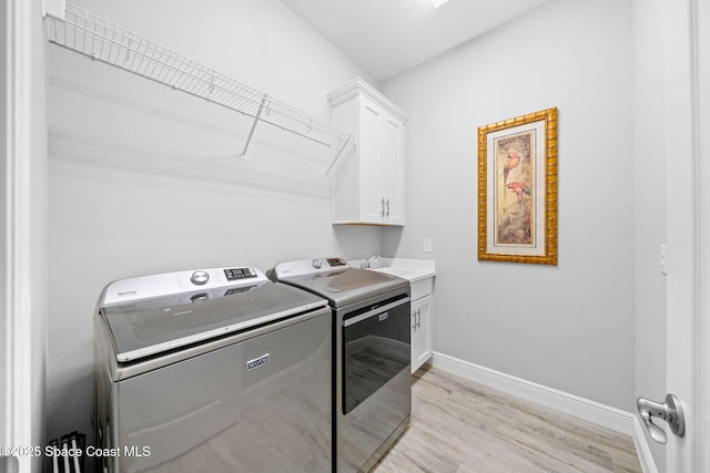 washroom with washing machine and clothes dryer, a sink, baseboards, light wood-style floors, and cabinet space