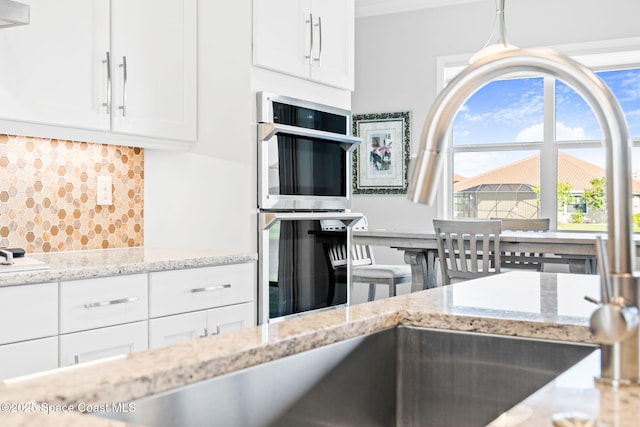 kitchen featuring crown molding, decorative backsplash, double oven, white cabinets, and light stone countertops