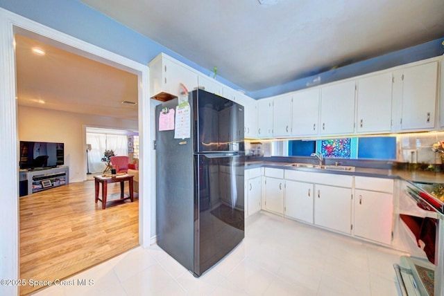 kitchen with a sink, freestanding refrigerator, white cabinetry, stainless steel electric range, and dark countertops
