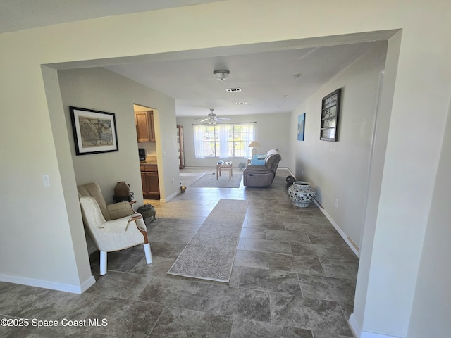 living area featuring stone finish floor, baseboards, a ceiling fan, and visible vents