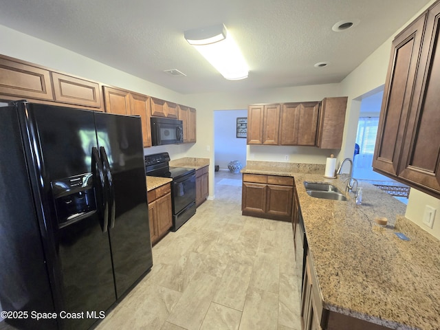 kitchen featuring visible vents, a sink, a textured ceiling, black appliances, and light stone countertops