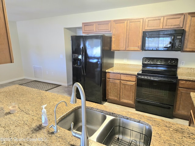 kitchen with visible vents, baseboards, a sink, black appliances, and light stone countertops