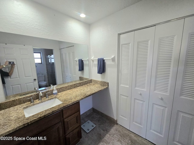 bathroom with a closet, baseboards, toilet, vanity, and tile patterned floors