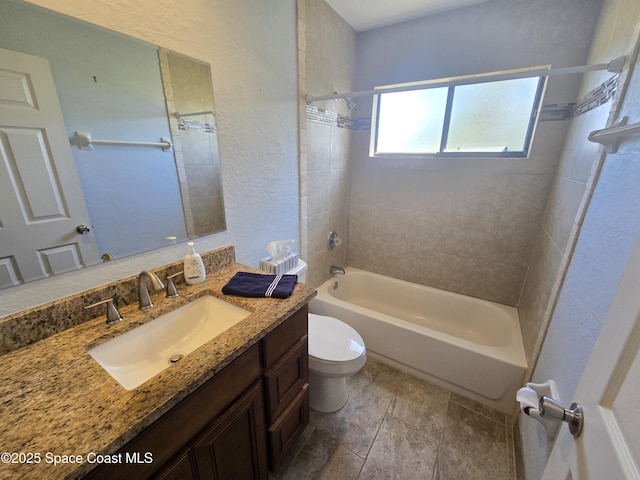 full bath featuring toilet, stone finish floor, a textured wall, shower / bath combination, and vanity