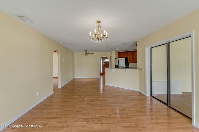 unfurnished living room featuring arched walkways, light wood finished floors, a notable chandelier, and visible vents