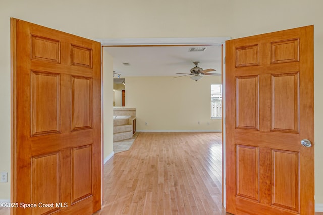 corridor with light wood-type flooring, baseboards, and visible vents