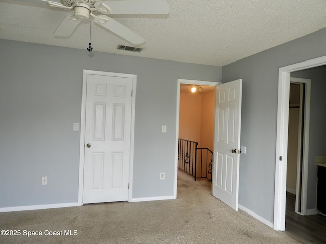 unfurnished bedroom featuring baseboards, a textured ceiling, visible vents, ceiling fan, and carpet