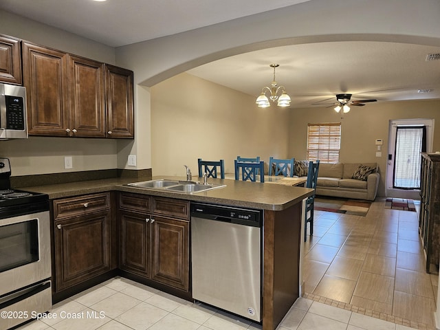 kitchen with a sink, arched walkways, dark countertops, and stainless steel appliances