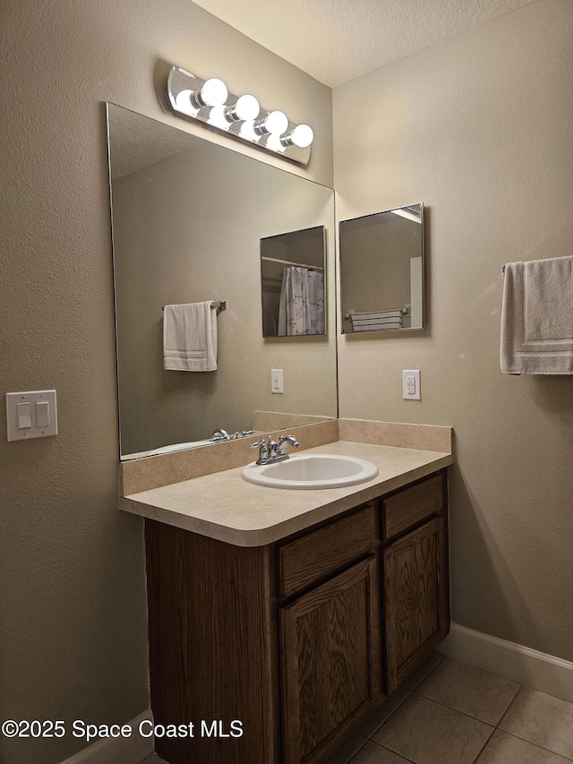 full bath featuring vanity, baseboards, a textured ceiling, and tile patterned floors