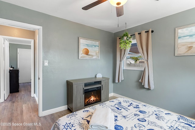 bedroom featuring a ceiling fan, wood finished floors, baseboards, and a glass covered fireplace