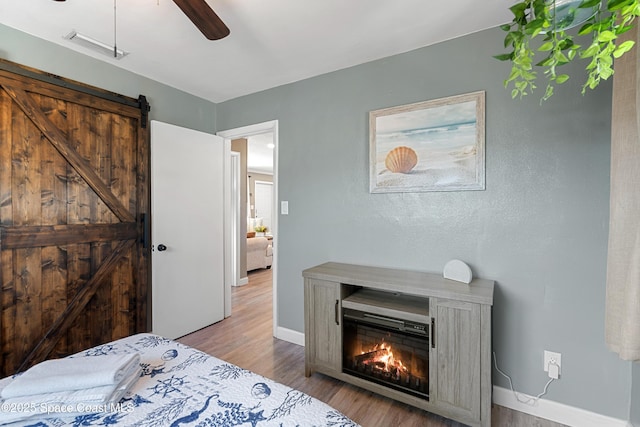 bedroom with baseboards, a barn door, visible vents, ceiling fan, and wood finished floors