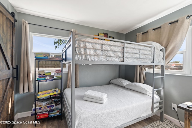 bedroom featuring a barn door, multiple windows, baseboards, and wood finished floors