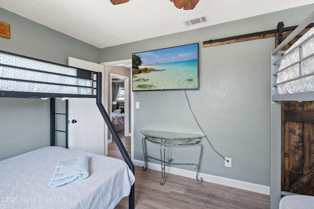 bedroom featuring a barn door, visible vents, baseboards, and wood finished floors