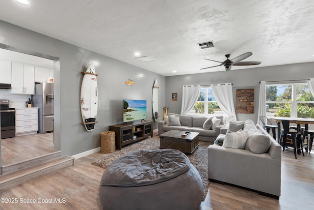 living area featuring light wood-type flooring, a ceiling fan, visible vents, and a textured ceiling