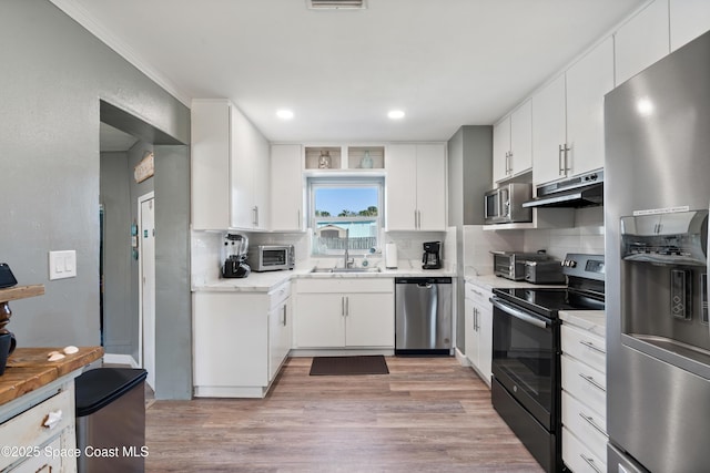 kitchen with appliances with stainless steel finishes, under cabinet range hood, decorative backsplash, light wood finished floors, and a sink