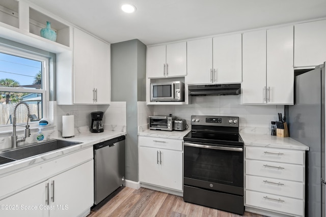 kitchen with a sink, under cabinet range hood, light wood finished floors, white cabinetry, and stainless steel appliances