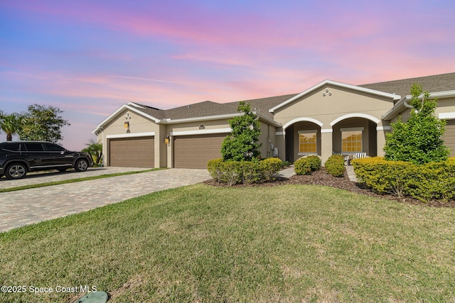 single story home with a garage, stucco siding, decorative driveway, and a yard