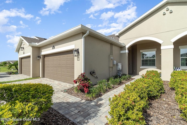 view of side of home with stucco siding, decorative driveway, and a garage