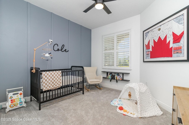 bedroom with ceiling fan, baseboards, a nursery area, and carpet floors