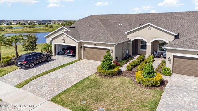 ranch-style house featuring a water view, decorative driveway, covered porch, an attached garage, and stucco siding