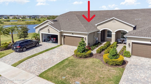 ranch-style house featuring a porch, stucco siding, decorative driveway, a water view, and an attached garage