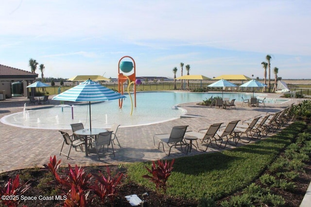 pool with a patio, a water play area, and fence